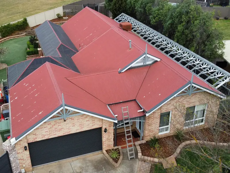 Before: a faded red corrugated roof with bare patches, seen from above