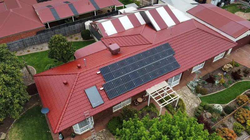 Red painted tile roof with solar panels on a single-storey home, aerial view